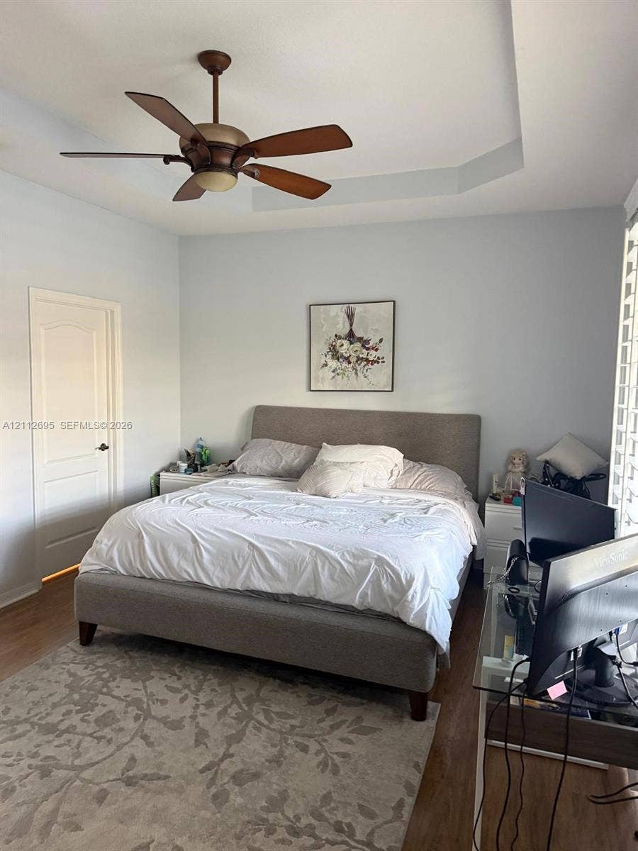 9812 SW Glenbrook Drive, Port St Lucie, FL 34987 Tray ceiling featuring a central five-blade ceiling fan with integrated lighting and wood-finish flooring