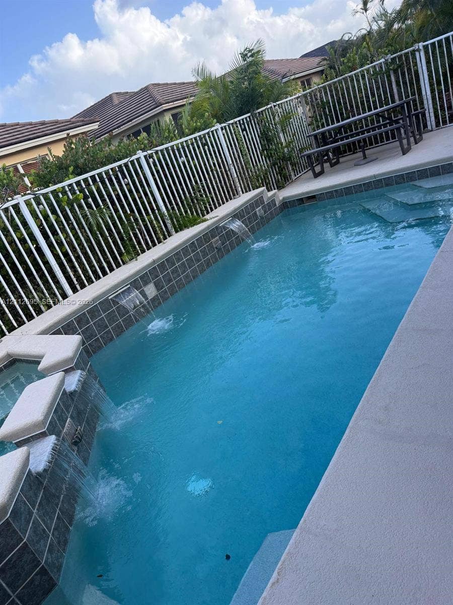 9812 SW Glenbrook Drive, Port St Lucie, FL 34987 Swimming pool featuring multiple water features, integrated spa, tiled finish, and perimeter metal fencing