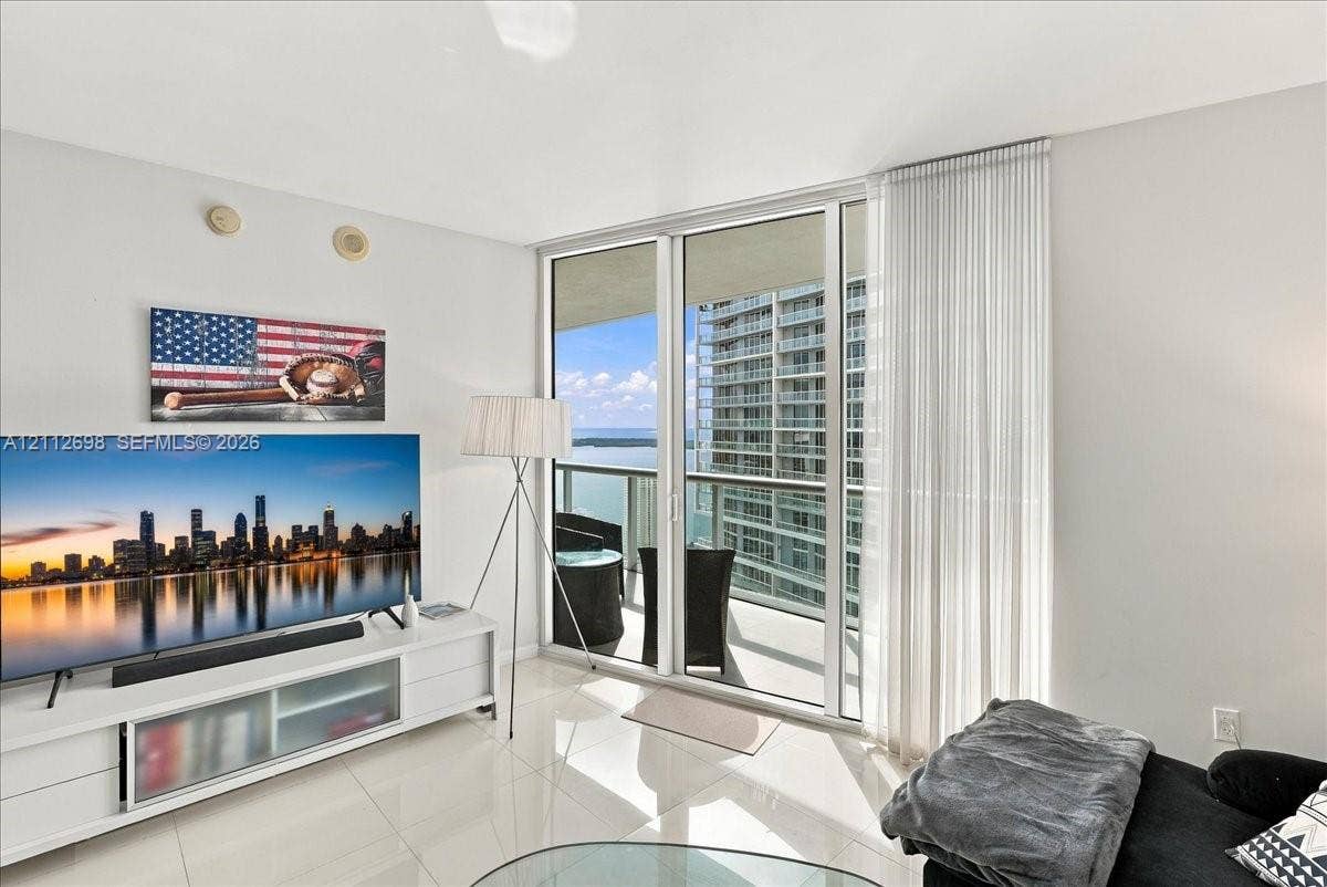 475 Brickell Avenue, #4511, Miami, FL 33131 Floor-to-ceiling glass sliding doors, polished tile flooring, and a covered balcony overlooking the water and metropolitan skyline
