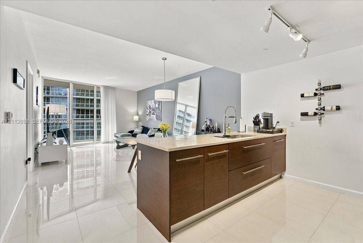 475 Brickell Avenue, #4511, Miami, FL 33131 Kitchen island featuring dark wood-finish cabinetry, neutral stone-finish countertops, and an integrated stainless steel undermount sink with a gooseneck faucet, complemented by large-format polished tile flooring