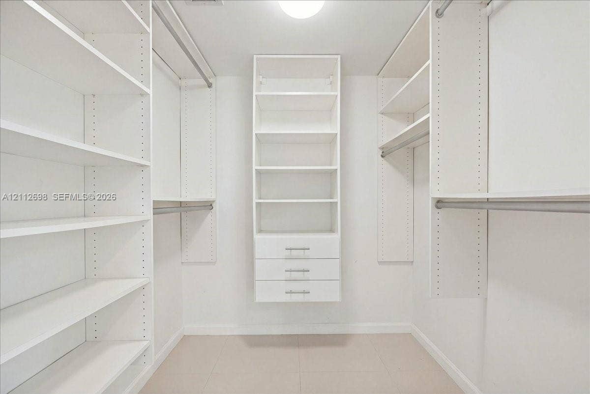 475 Brickell Avenue, #4511, Miami, FL 33131 Walk-in closet featuring white built-in shelving, triple-drawer storage unit, metal hanging rods, and tile flooring