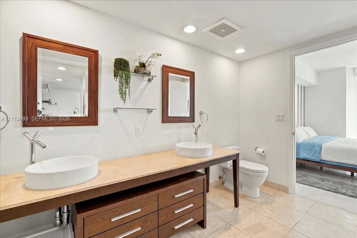 475 Brickell Avenue, #4511, Miami, FL 33131 Double vanity featuring a light-toned countertop, two white vessel sinks, wood-finish cabinetry, and wall-mounted faucets