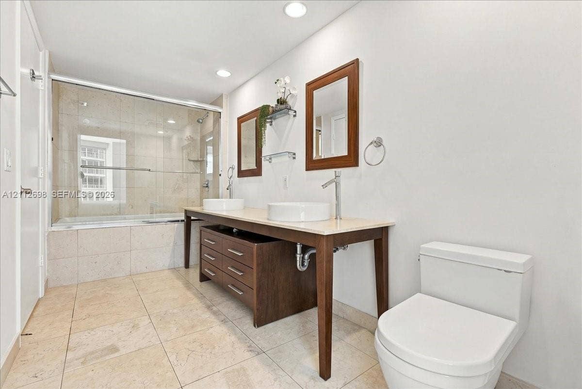 475 Brickell Avenue, #4511, Miami, FL 33131 Double vanity with dual vessel sinks, stone-surface countertop, dark wood-finish cabinetry, and a glass-enclosed shower with tile surround