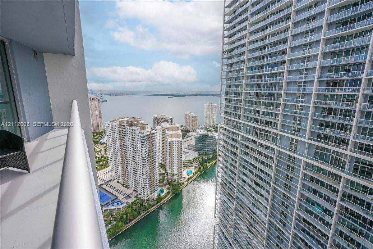 475 Brickell Avenue, #4511, Miami, FL 33131 Covered balcony featuring glass and metal railings, overlooking urban high-rise buildings, a waterway, and a bay