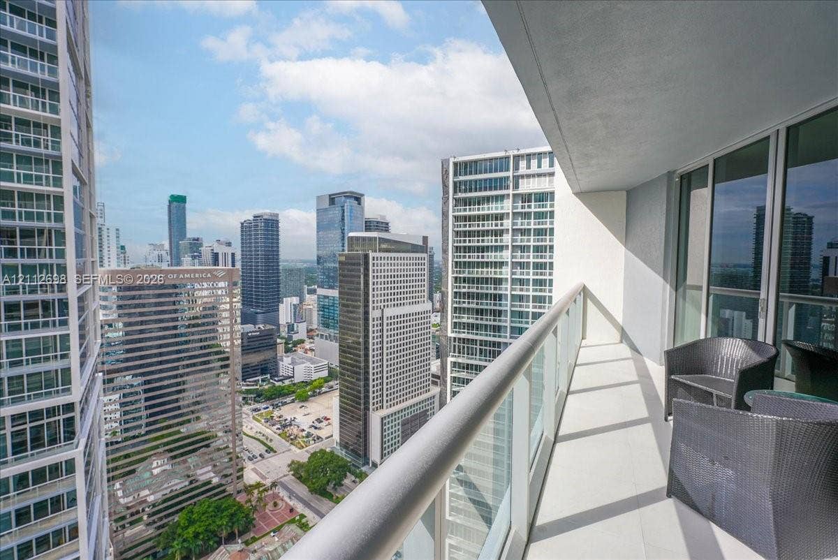 475 Brickell Avenue, #4511, Miami, FL 33131 Covered balcony featuring a metal railing with glass panels, concrete flooring, and urban high-rise surroundings