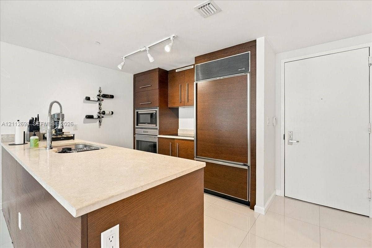 475 Brickell Avenue, #4511, Miami, FL 33131 Kitchen featuring wood-finish cabinetry, a paneled refrigerator, integrated wall oven, neutral stone-finish countertops, and track lighting