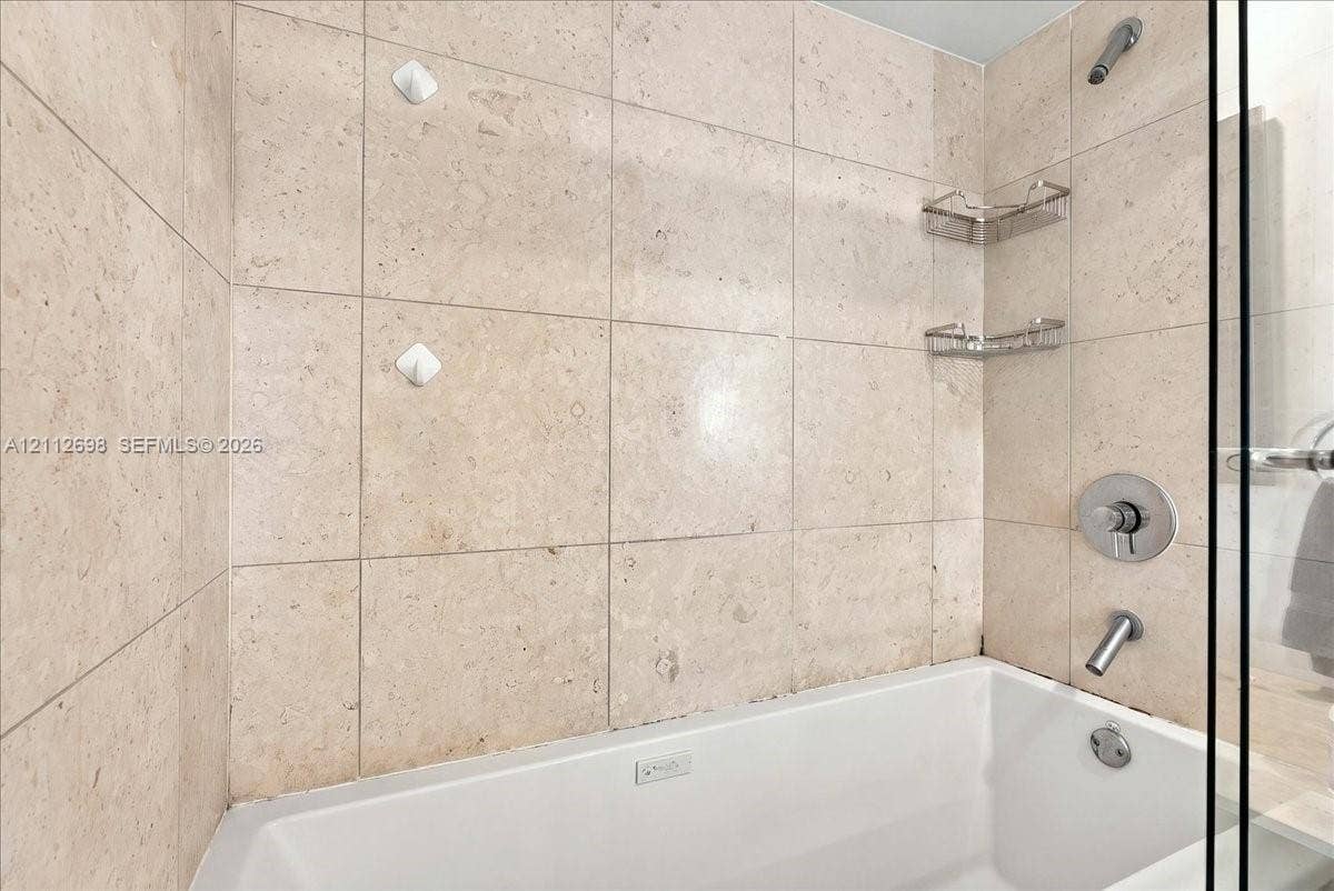 475 Brickell Avenue, #4511, Miami, FL 33131 Shower and bathtub combination featuring large-format stone-finish tile surround, polished chrome fixtures, and built-in metal shelving