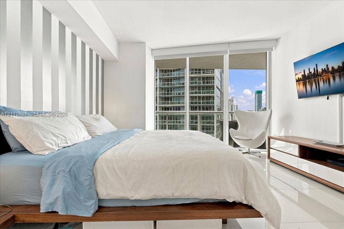 475 Brickell Avenue, #4511, Miami, FL 33131 Floor-to-ceiling glass windows, wall-mounted television, vertical-paneled accent wall, and polished white tile flooring