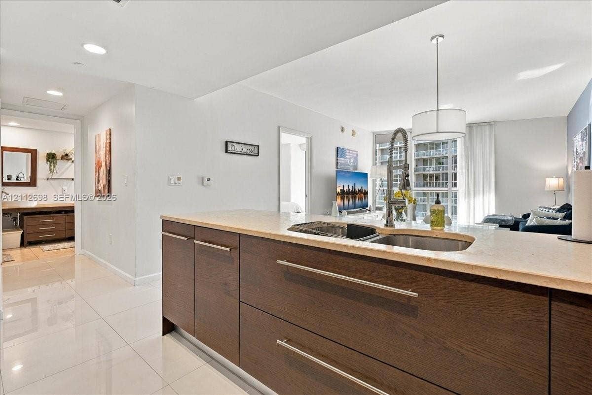 475 Brickell Avenue, #4511, Miami, FL 33131 Kitchen island featuring dark wood-finish cabinetry, solid surface countertops, an undermount stainless steel double-basin sink, and a high-arc gooseneck faucet