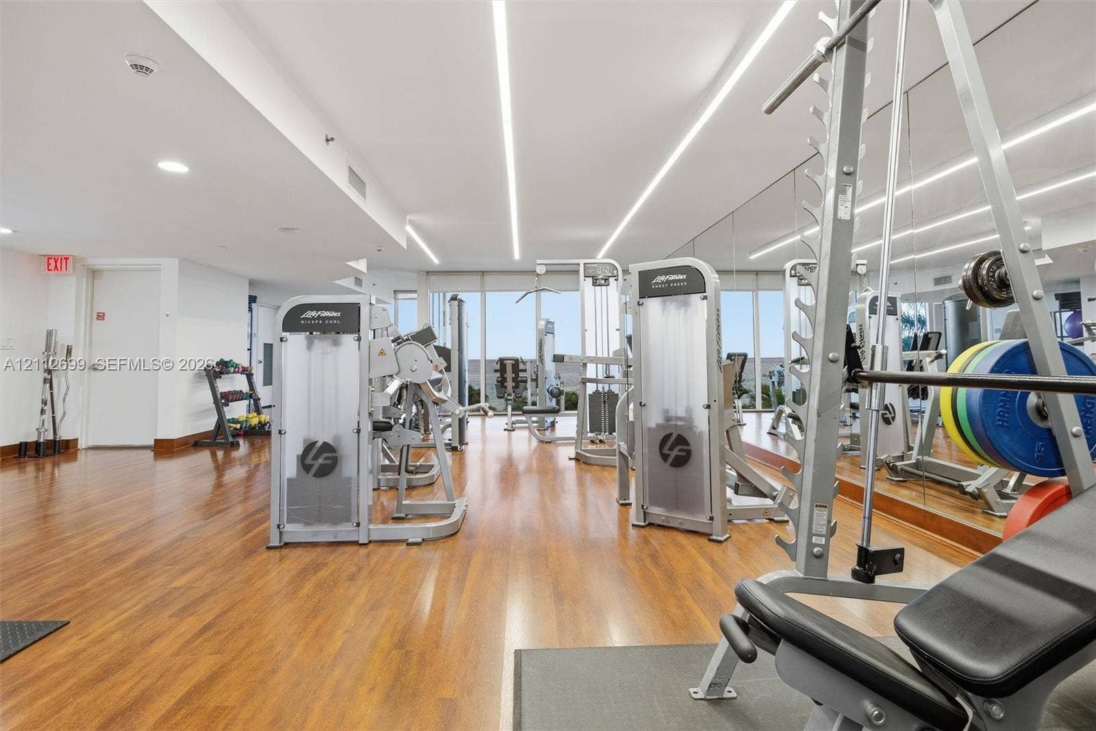 19111 Collins Avenue, #505, Sunny Isles Beach, FL 33160 Fitness facility featuring wood-finish flooring, floor-to-ceiling mirrored walls, and recessed linear lighting