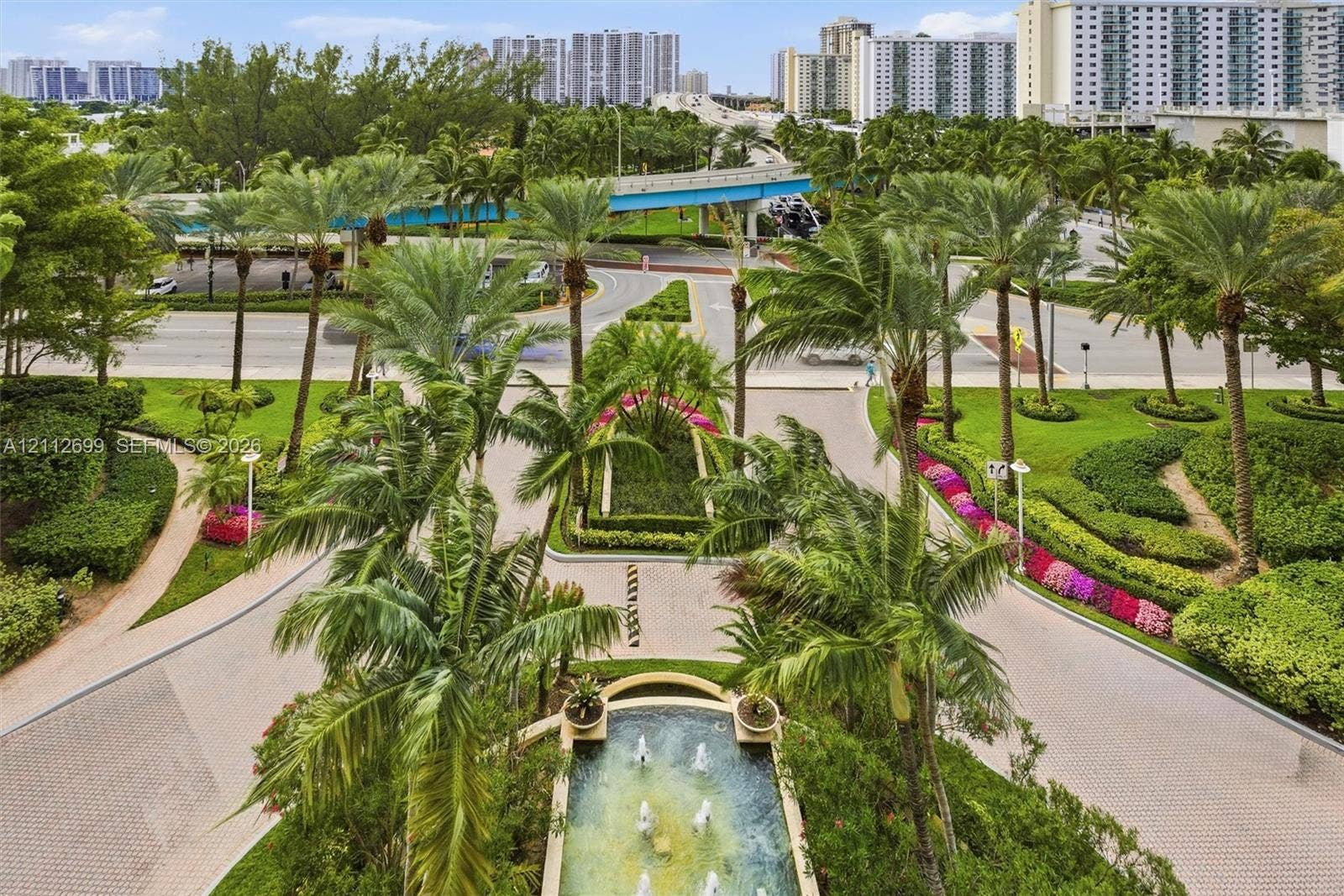 19111 Collins Avenue, #505, Sunny Isles Beach, FL 33160 Landscaped motor court featuring a central tiered fountain, paver stone driveway, mature palm trees, and manicured tropical gardens