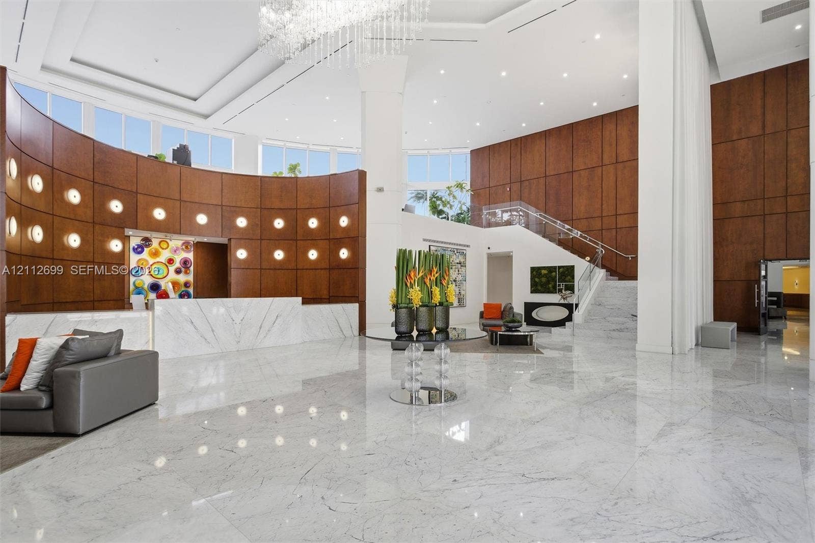 19111 Collins Avenue, #505, Sunny Isles Beach, FL 33160 Grand entrance featuring high ceilings, polished stone flooring, curved wood-paneled walls, a statement crystal chandelier, and a built-in stone reception desk