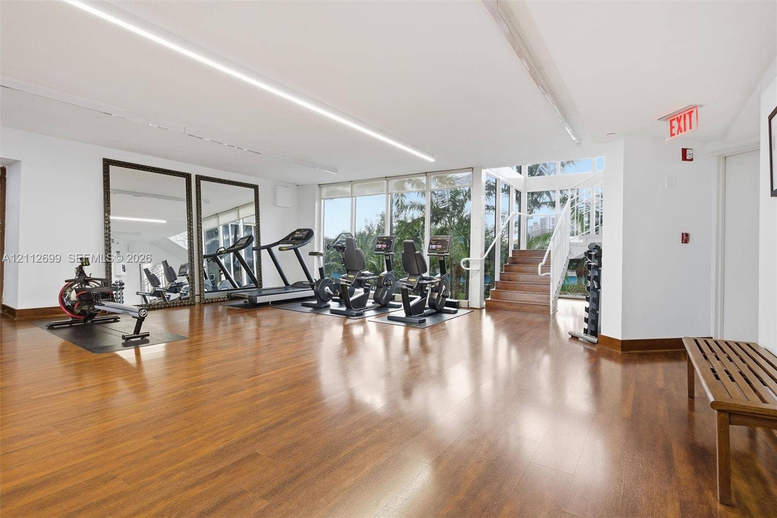 19111 Collins Avenue, #505, Sunny Isles Beach, FL 33160 Fitness facility featuring wood-finish flooring, floor-to-ceiling windows, full-wall mirrors, and a wooden staircase with a white metal railing