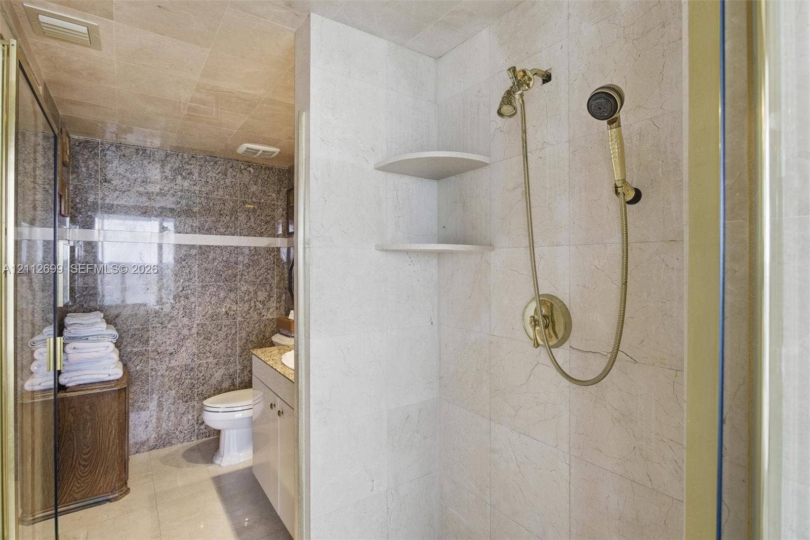 19111 Collins Avenue, #505, Sunny Isles Beach, FL 33160 Walk-in shower enclosure featuring floor-to-ceiling neutral tile, built-in shelving, and gold-finish hardware including a handheld showerhead