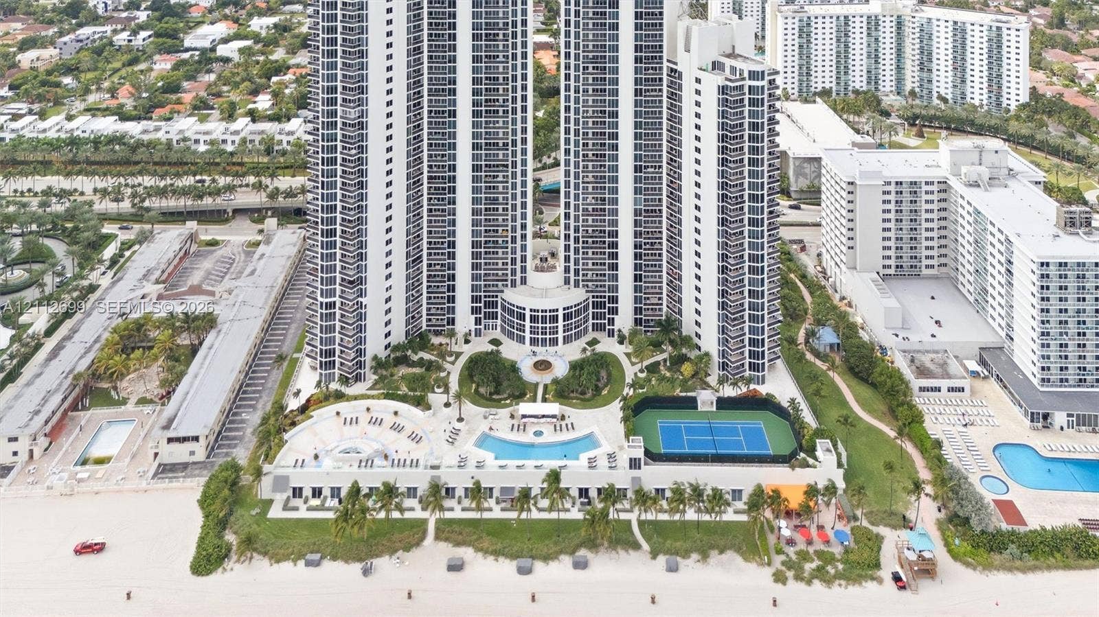 19111 Collins Avenue, #505, Sunny Isles Beach, FL 33160 High-rise residential tower featuring a direct beachfront location, swimming pool with surrounding deck, tennis court, and professionally landscaped grounds