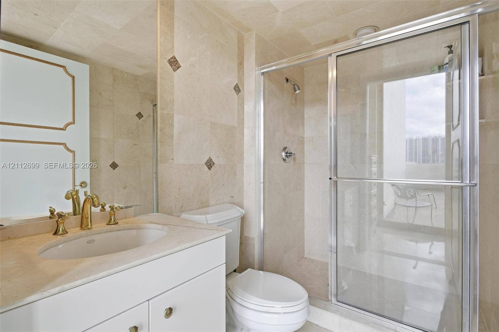19111 Collins Avenue, #505, Sunny Isles Beach, FL 33160 Stone-tiled bathroom featuring a vanity with a drop-in sink, gold-toned hardware, large wall-mounted mirror, and a walk-in shower with glass enclosure