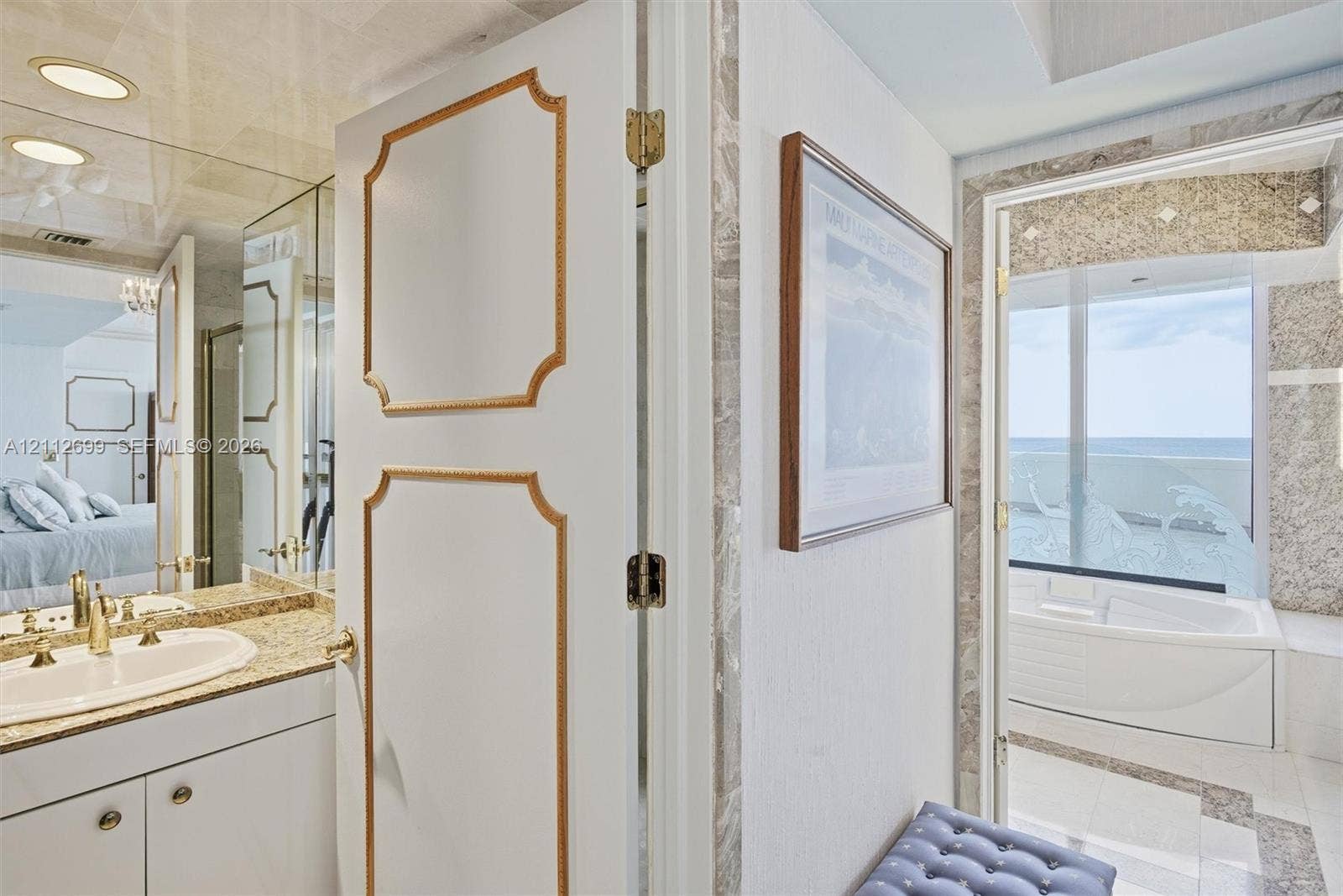 19111 Collins Avenue, #505, Sunny Isles Beach, FL 33160 Vanity featuring an oval undermount sink, stone countertop, and full-height mirrored wall, paired with a jetted soaking tub positioned against a large window with ocean scenery