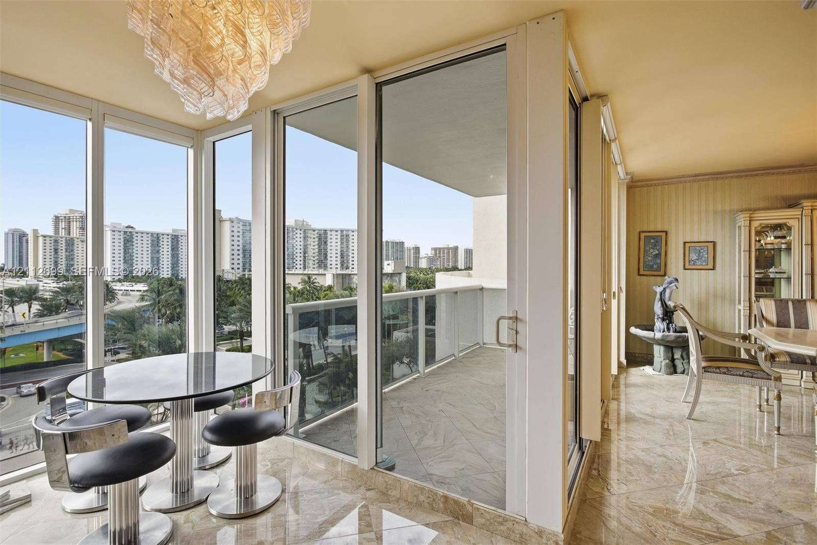 19111 Collins Avenue, #505, Sunny Isles Beach, FL 33160 Floor-to-ceiling glass paneling, sliding glass door access to a private balcony, polished stone-finish flooring, and a decorative crystal chandelier