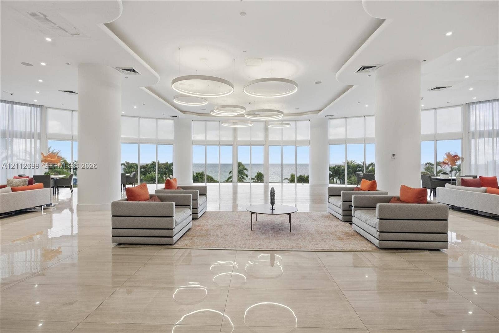 19111 Collins Avenue, #505, Sunny Isles Beach, FL 33160 Expansive open-concept space featuring polished stone flooring, floor-to-ceiling windows, sculptural circular pendant lighting, recessed tray ceiling details, and structural support columns