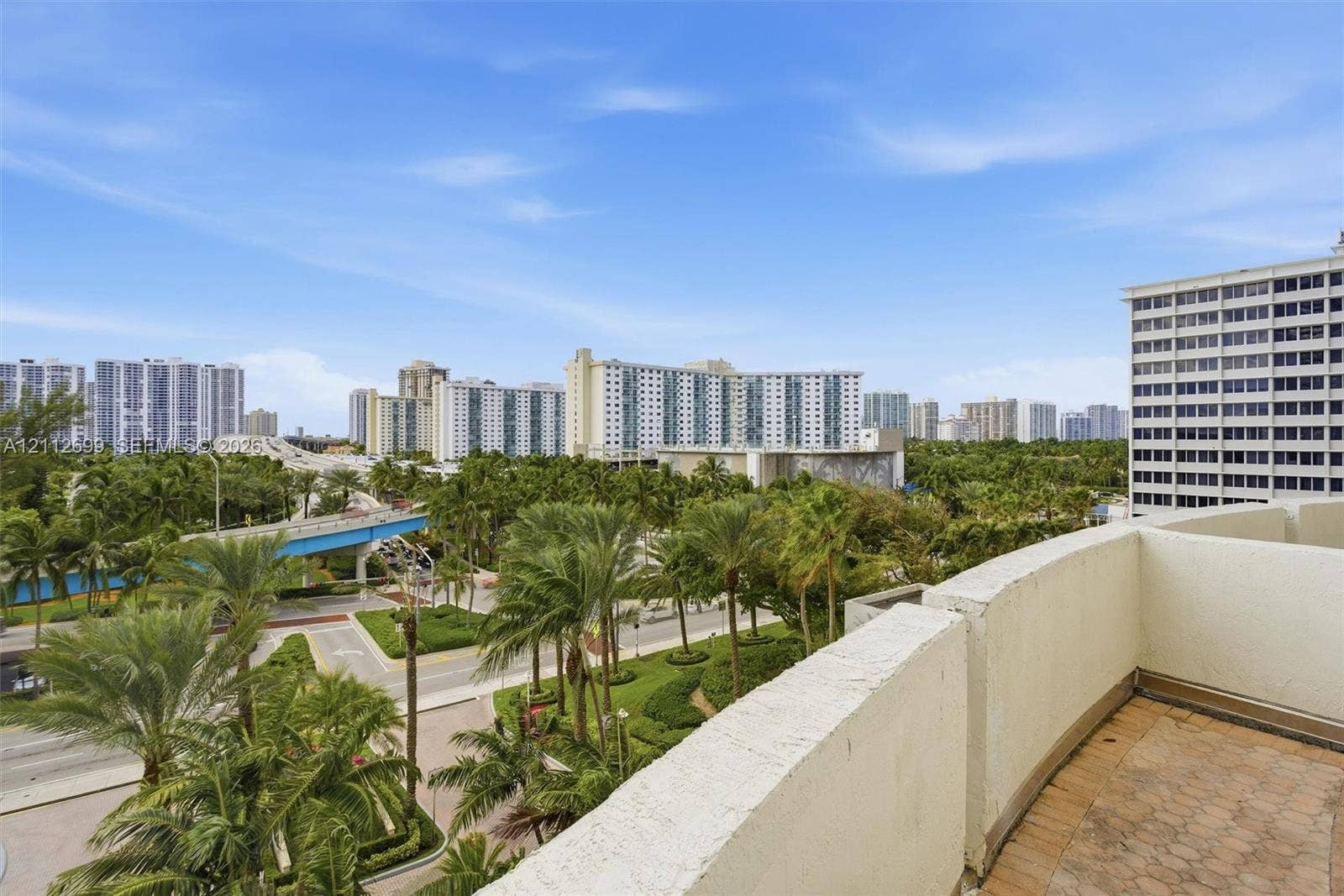 19111 Collins Avenue, #505, Sunny Isles Beach, FL 33160 Balcony with textured masonry walls and tiled flooring overlooking an urban landscape featuring mature palm trees and multi-story structures