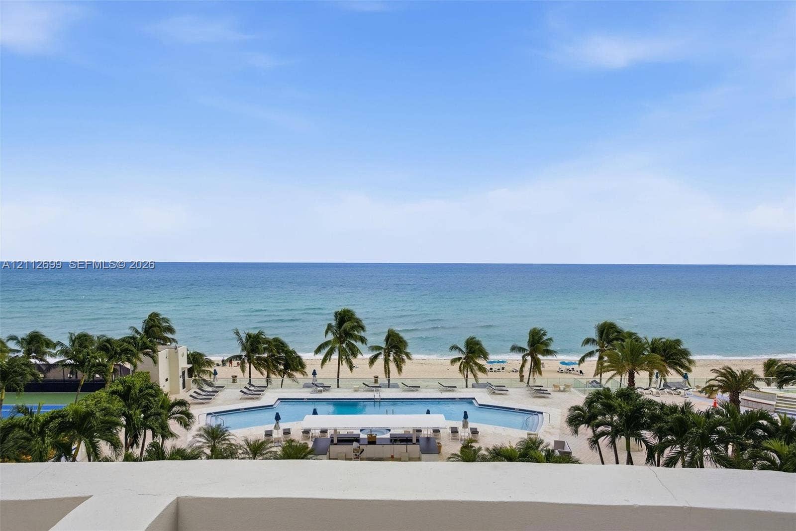 19111 Collins Avenue, #505, Sunny Isles Beach, FL 33160 Oceanfront terrace featuring a concrete parapet, overlooking a resort-style swimming pool, lush palm trees, and sand beach
