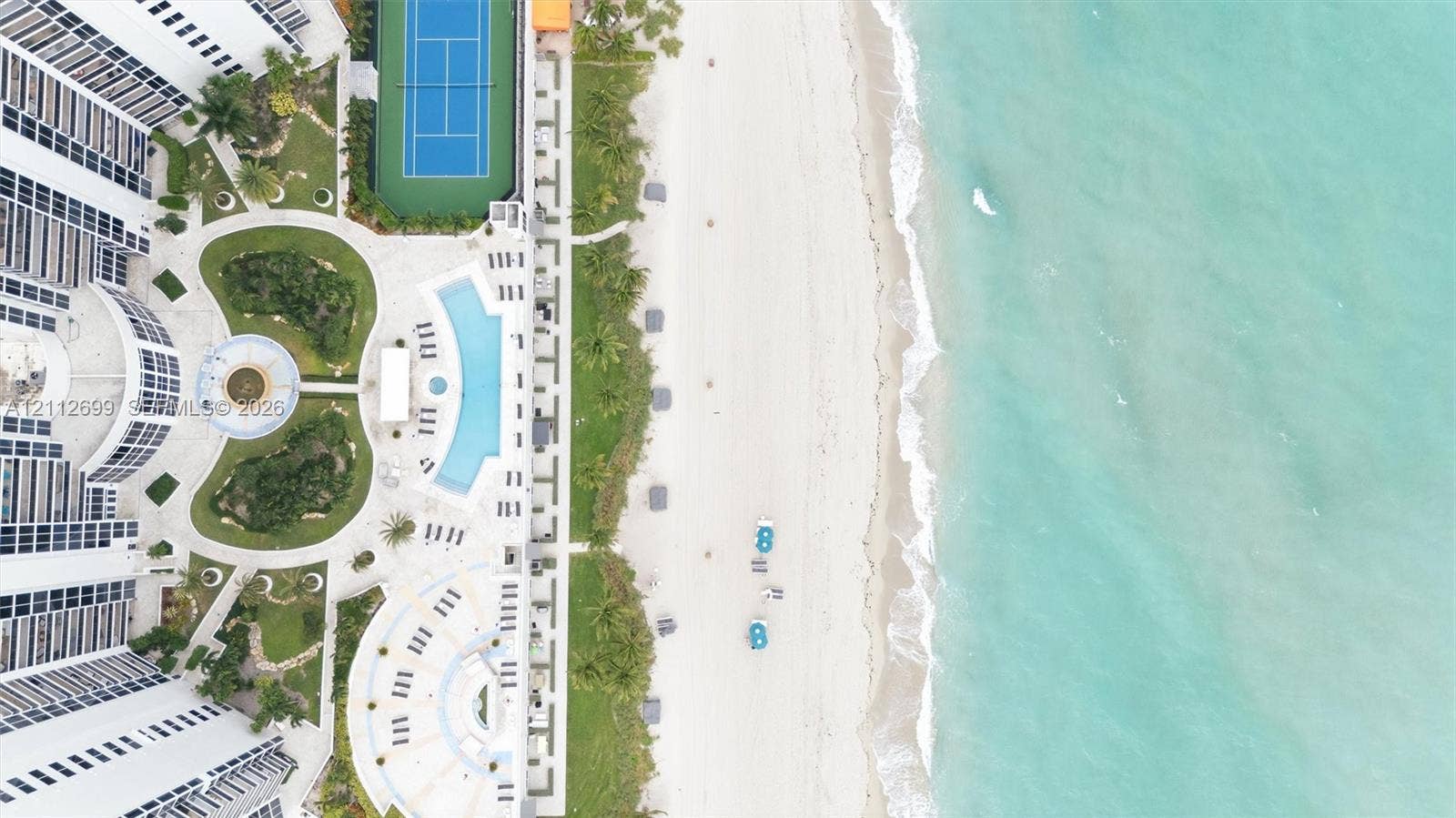 19111 Collins Avenue, #505, Sunny Isles Beach, FL 33160 Aerial perspective of a coastal property featuring direct beach access, a swimming pool, a tennis court, and manicured landscaping