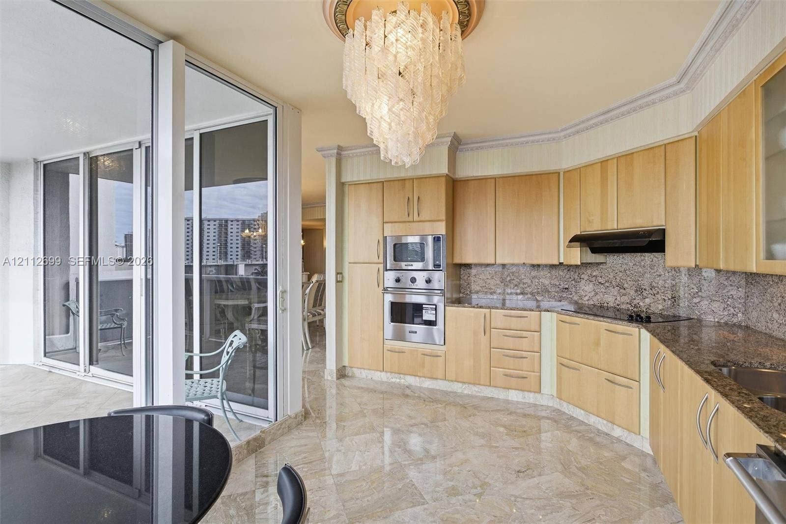 19111 Collins Avenue, #505, Sunny Isles Beach, FL 33160 Kitchen featuring light-finish cabinetry, stone countertops with a matching full-height backsplash, polished stone flooring, integrated stainless steel appliances, and a decorative crystal chandelier with an ornate ceiling medallion