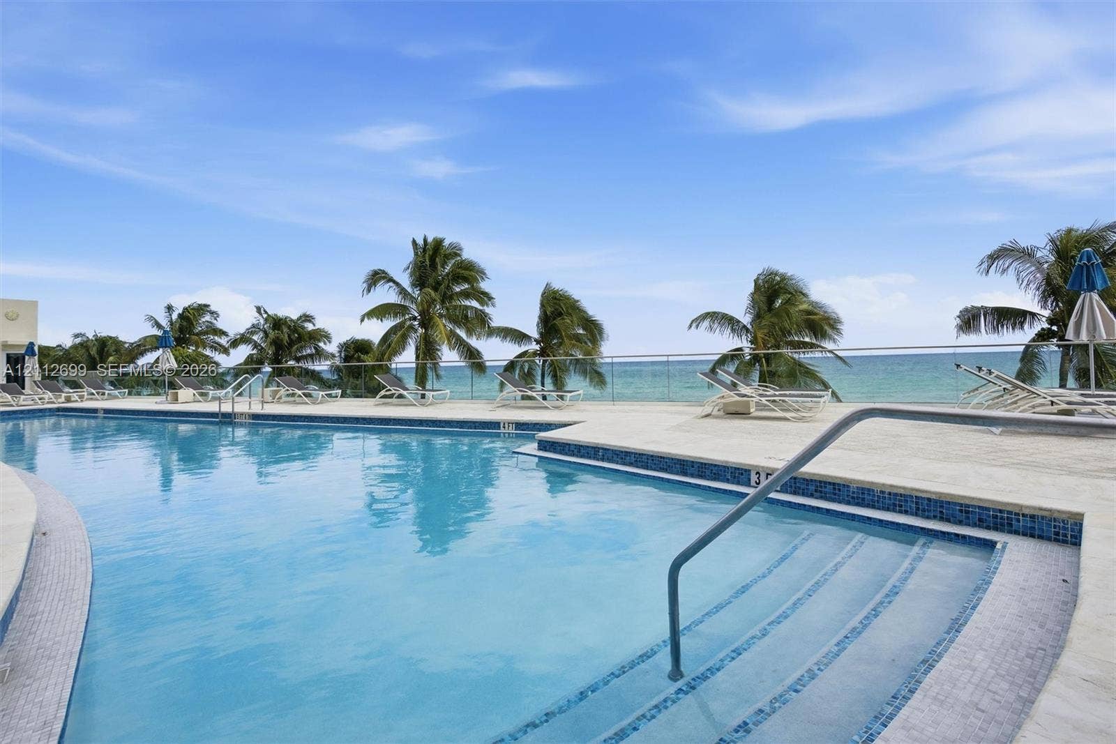 19111 Collins Avenue, #505, Sunny Isles Beach, FL 33160 Swimming pool with mosaic tile border, light-toned stone decking, metal handrail, and transparent glass railing overlooking the ocean