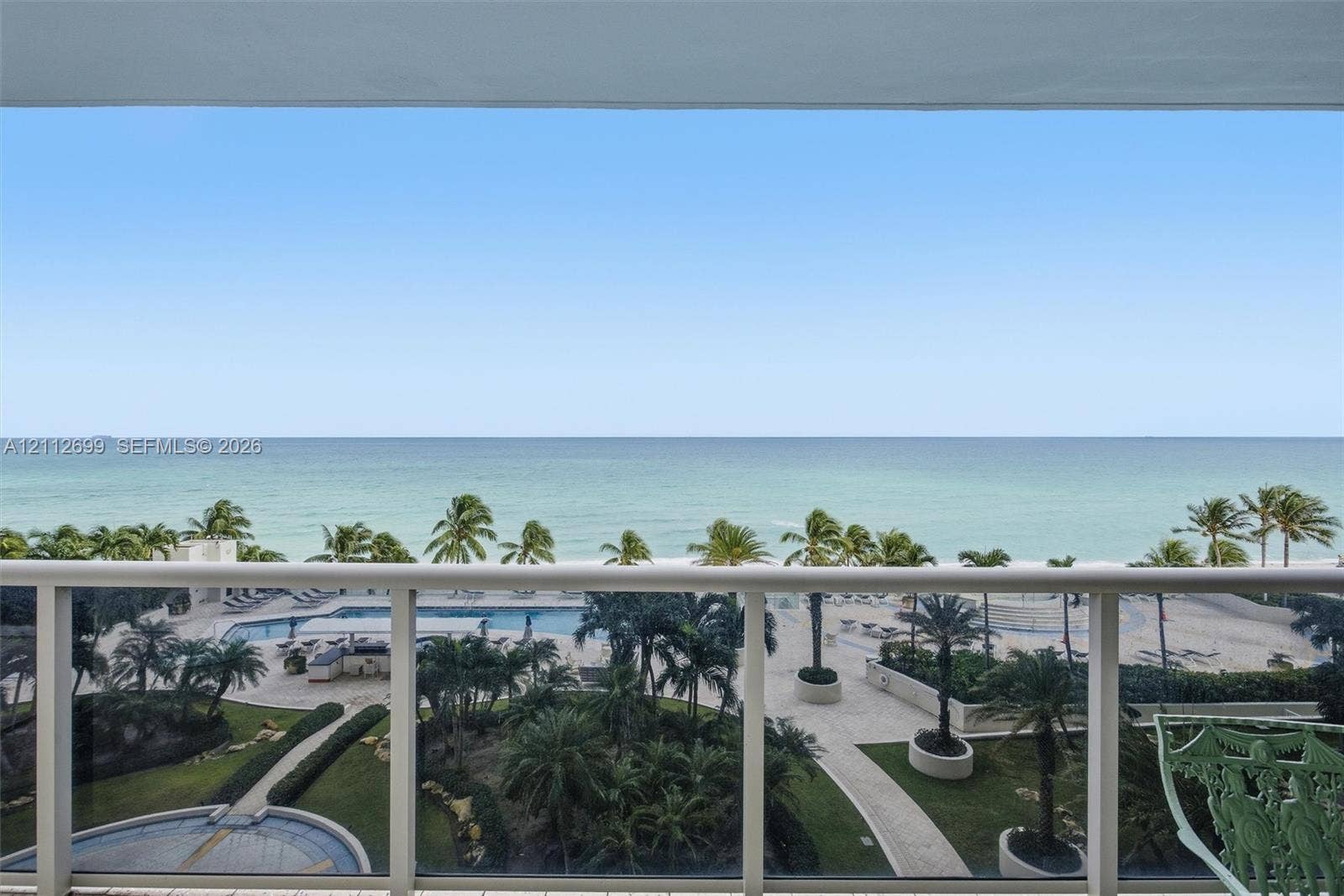 19111 Collins Avenue, #505, Sunny Isles Beach, FL 33160 Covered balcony featuring white metal railings, overlooking an oceanfront landscape with a swimming pool, paved walkways, and palm trees