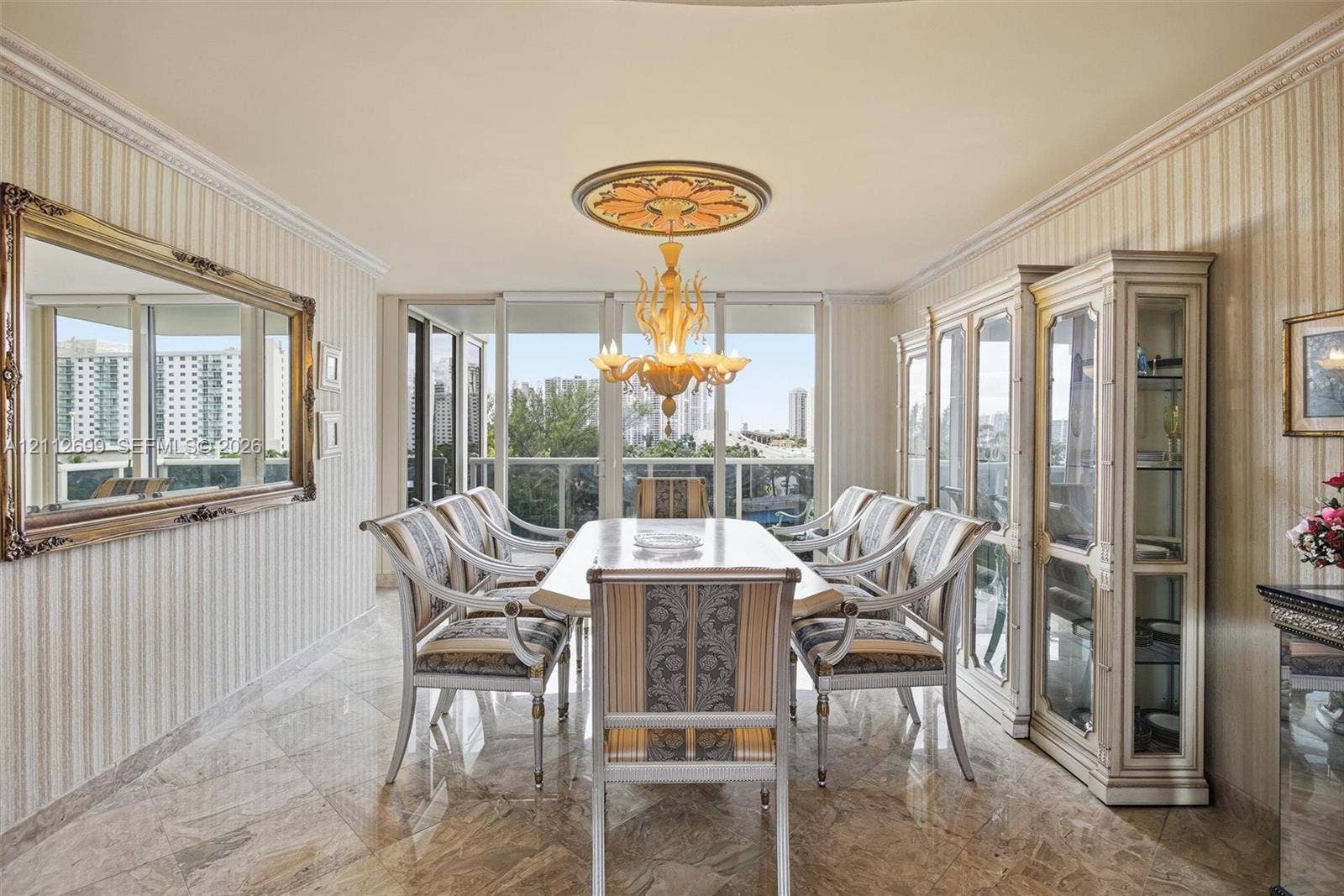 19111 Collins Avenue, #505, Sunny Isles Beach, FL 33160 Dining area featuring polished stone flooring, custom built-in cabinetry, crown molding, a decorative ceiling medallion, and a chandelier