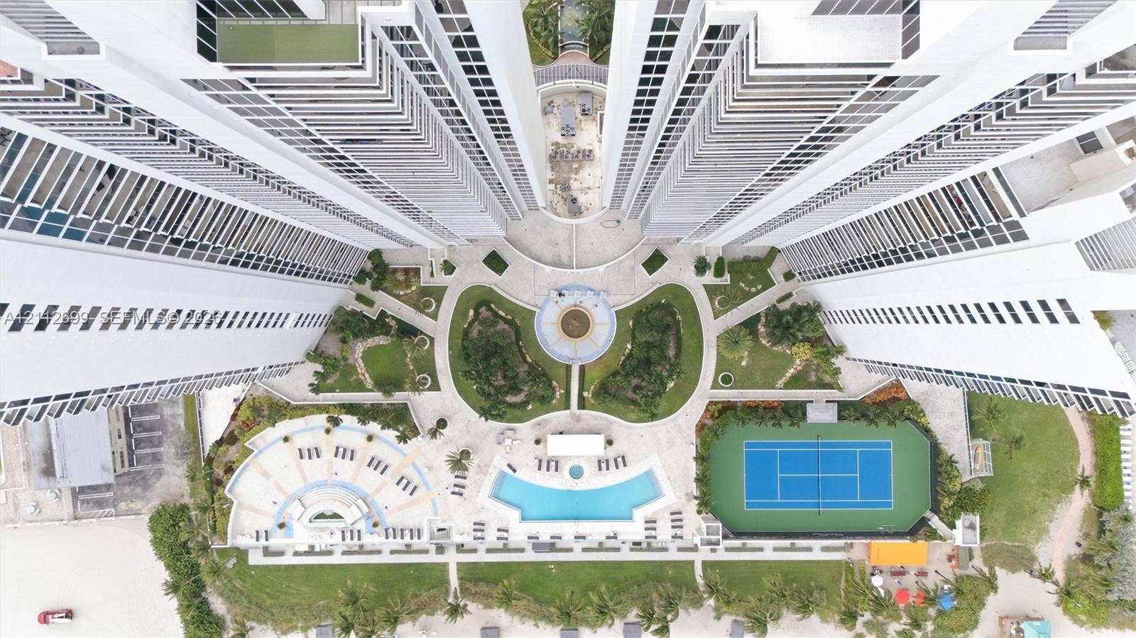 19111 Collins Avenue, #505, Sunny Isles Beach, FL 33160 Aerial perspective of high-rise condominium complex featuring a central courtyard with structured landscaping, a swimming pool, a tennis court, and paved pedestrian paths