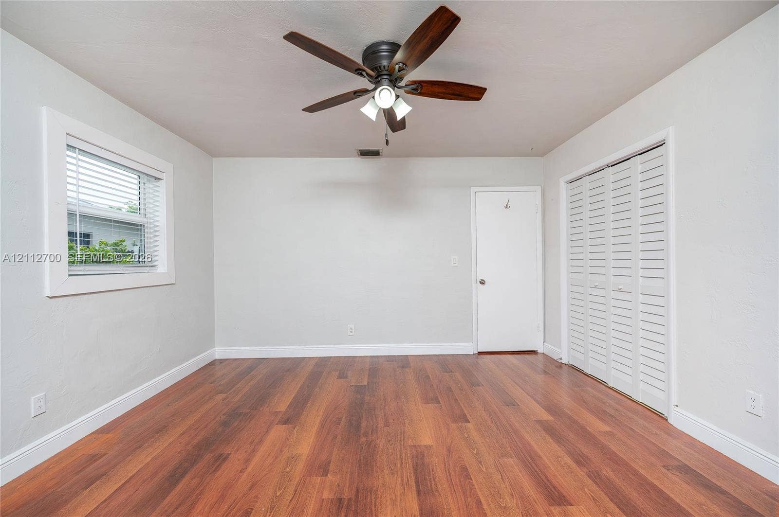 Wood-finish flooring, ceiling fan with integrated lighting, dual-panel closet doors, and window with blinds