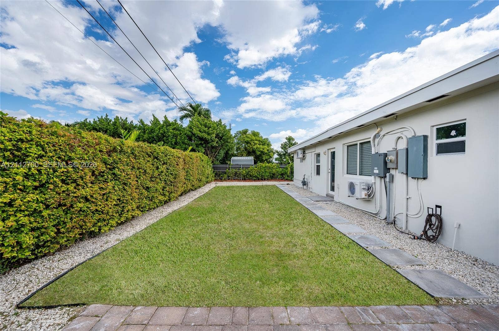 Rear yard featuring a manicured lawn, stone paver pathway, and established privacy hedges