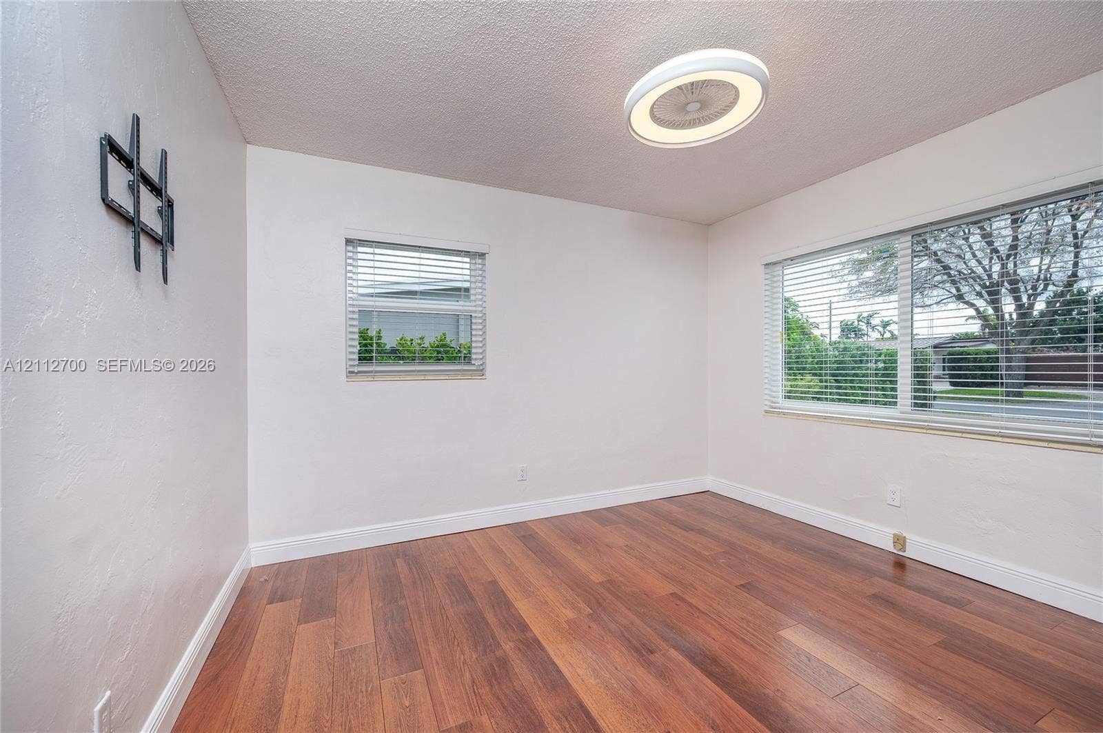 Room featuring wood-finish flooring, two large windows with horizontal blinds, and a circular flush-mount LED light fixture
