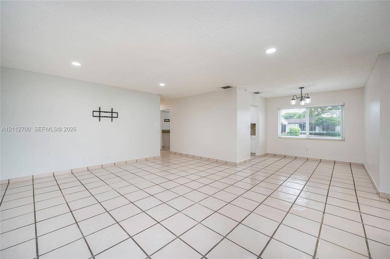 Open-concept room featuring light-toned tile flooring, recessed ceiling lighting, a multi-arm chandelier, and a large window