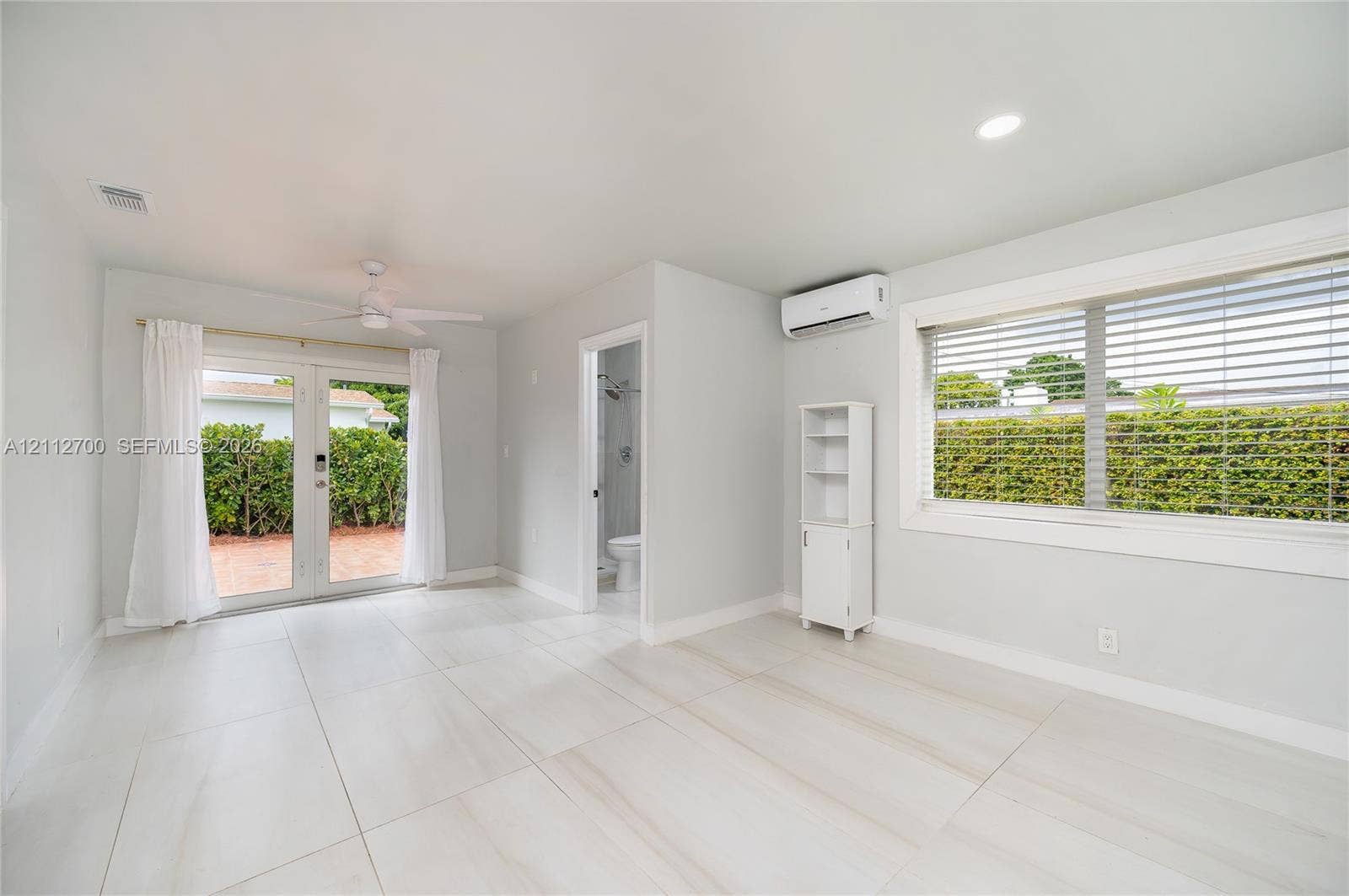 Large-format tile flooring, recessed lighting, ceiling fan, wall-mounted ductless climate control unit, and glass-paned double doors