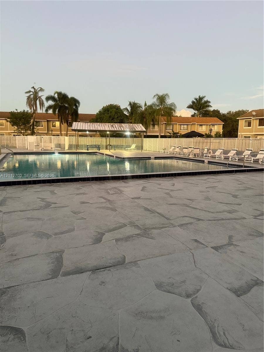 Swimming pool with stamped concrete deck, metal-roofed cabana, and perimeter fencing