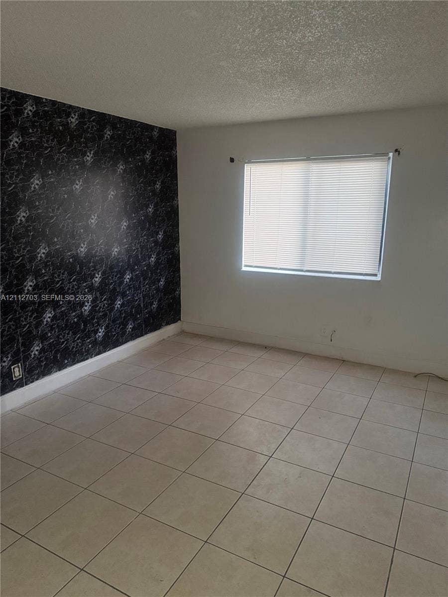 Room featuring large-format ceramic tile flooring, a black-and-white patterned accent wall, and a horizontal window with integrated blinds