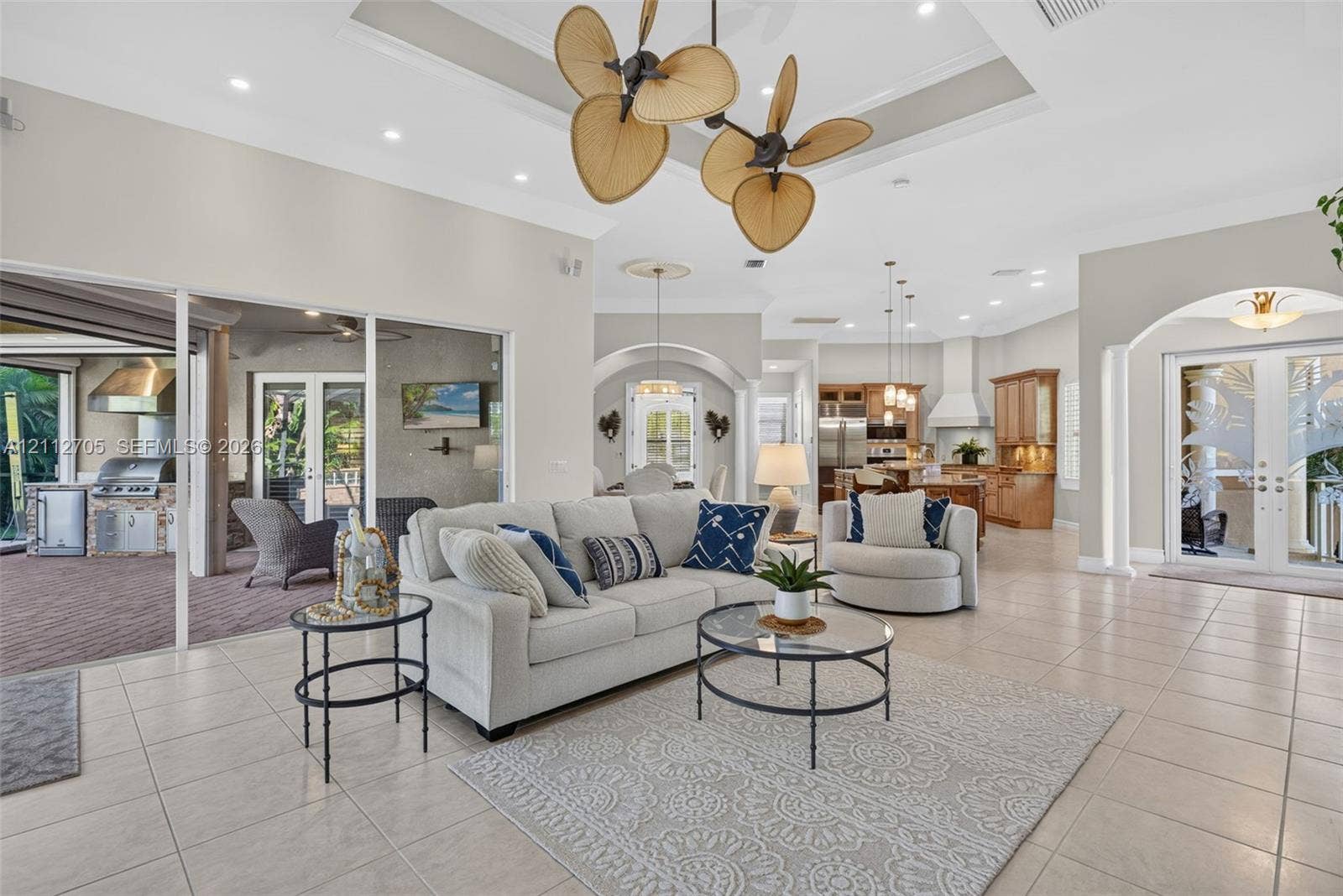 15600 Catalpa Cove Drive, Naples, FL 33908 Tray ceiling with recessed lighting, multi-blade sculptural chandelier, tile flooring, arched architectural transitions, and expansive sliding glass doors