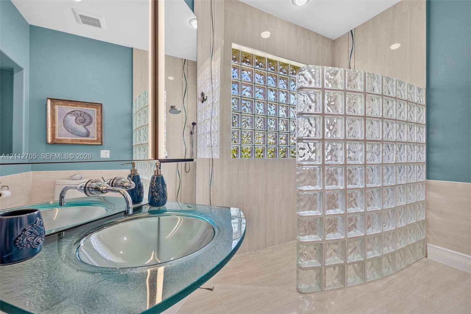 15600 Catalpa Cove Drive, Naples, FL 33908 Glass block privacy wall, custom molded glass vanity top with integrated sink, polished chrome widespread faucet, and large-format tile wall cladding