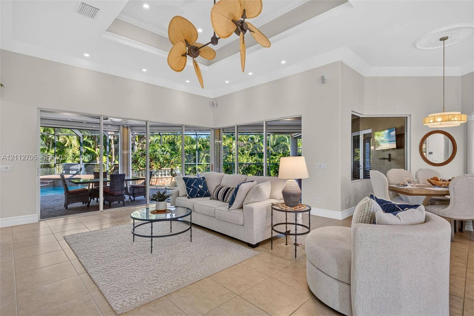 15600 Catalpa Cove Drive, Naples, FL 33908 Tray ceiling with recessed lighting, multi-blade sculptural ceiling fan, large-format tile flooring, and expansive floor-to-ceiling glass sliding doors