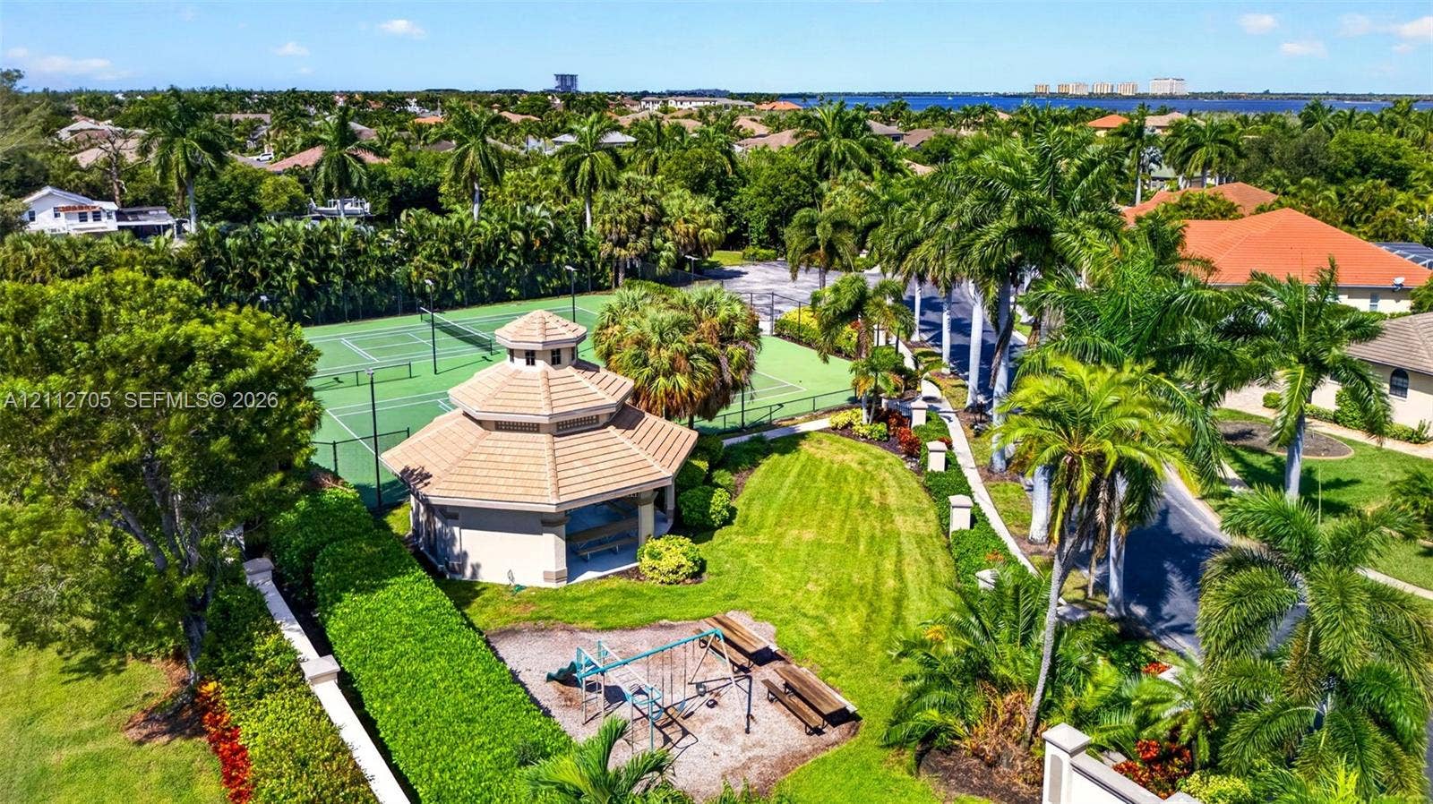 15600 Catalpa Cove Drive, Naples, FL 33908 Community grounds featuring a tennis court, a roofed gazebo with tile-style roofing, and mature palm trees