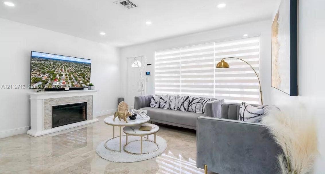 Bright interior featuring large-format tile flooring, recessed lighting, and a fireplace with a stone-textured surround