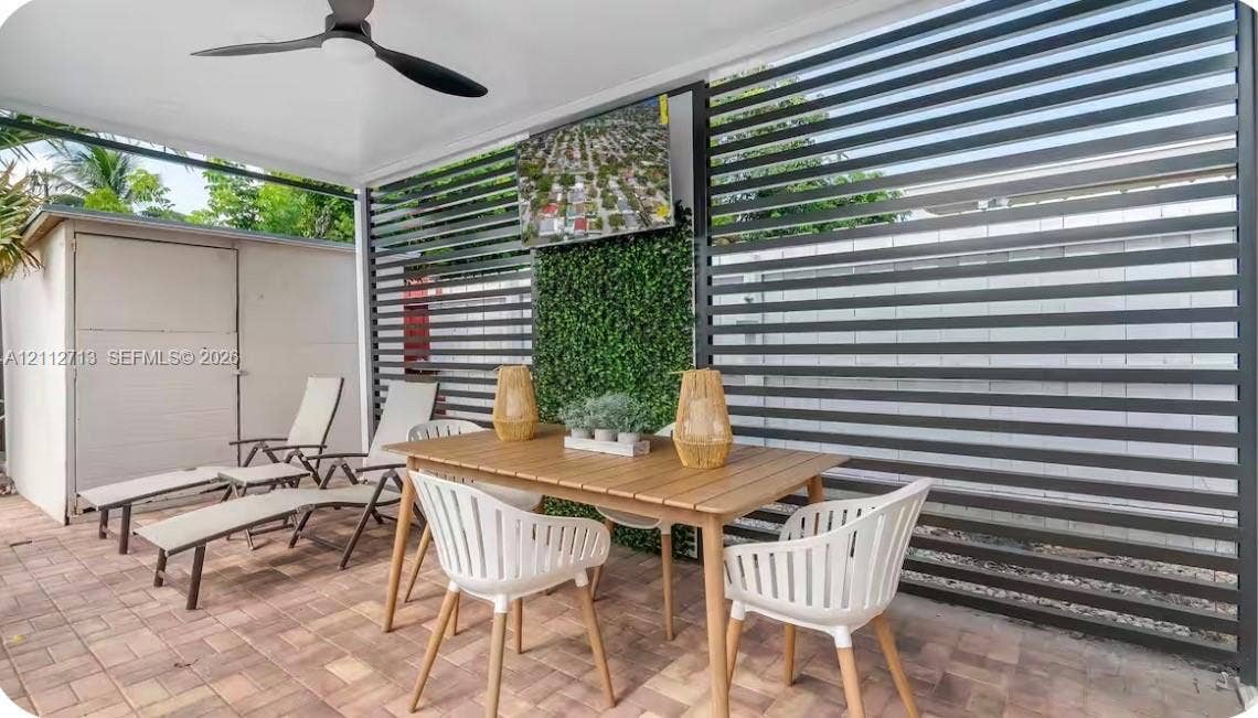 Covered patio featuring paver flooring, horizontal slat privacy screening, an integrated artificial greenery wall, and a ceiling-mounted fan
