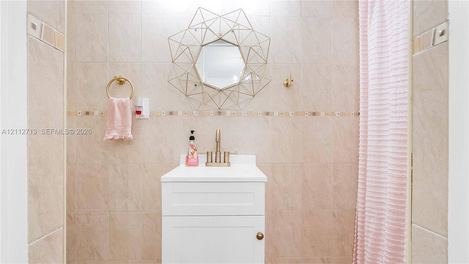 White vanity with a rectangular sink, metallic faucet, wall-mounted circular geometric mirror, and floor-to-ceiling tile featuring a decorative accent border
