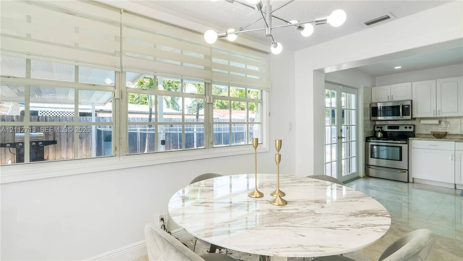 Multi-pane window wall with roller shades, modern multi-arm sputnik chandelier, white cabinetry, stainless steel appliances, and tile flooring