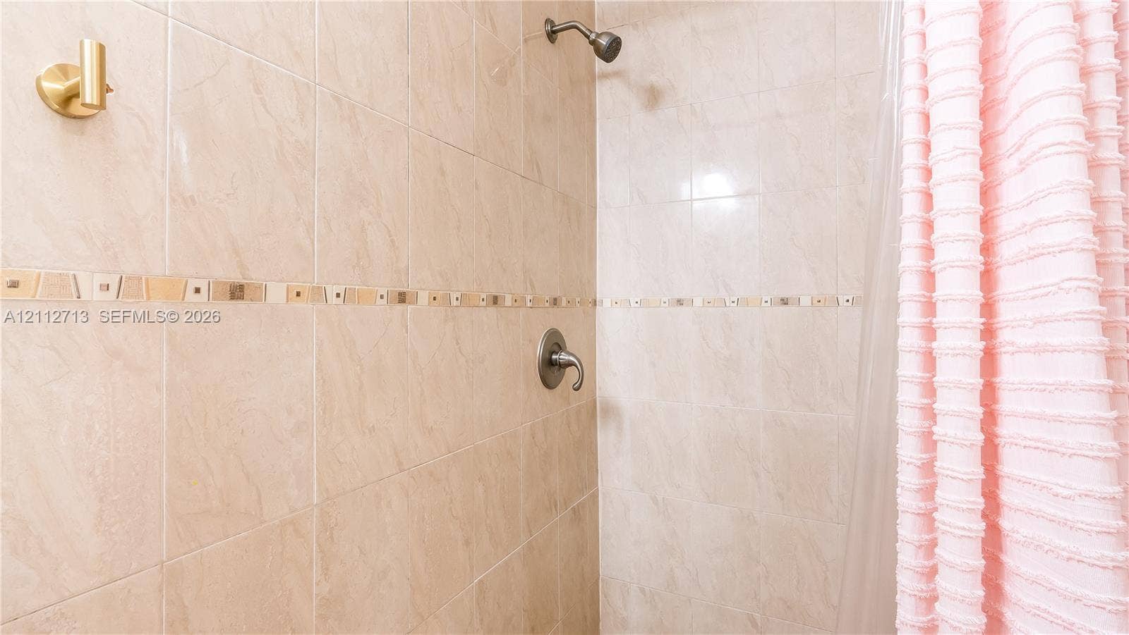 Shower enclosure featuring large-format beige wall tiling, a decorative glass and stone mosaic accent border, and a metallic single-handle pressure-balance valve