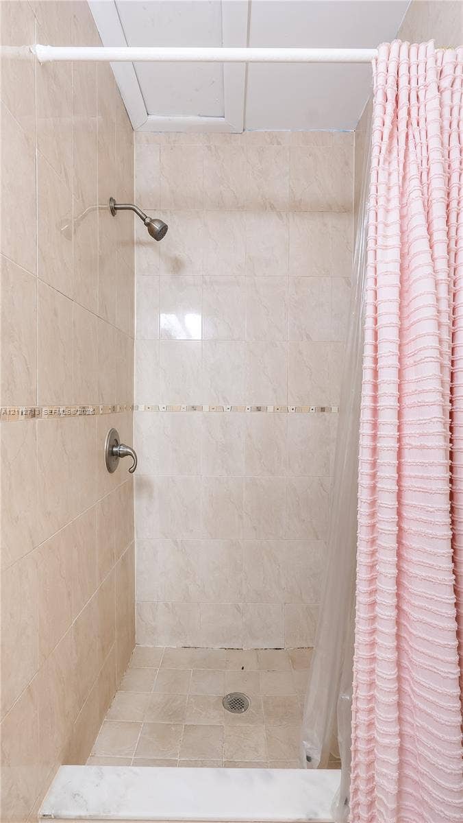 Walk-in shower featuring beige wall and floor tile, a decorative mosaic tile accent border, and a metallic shower fixture