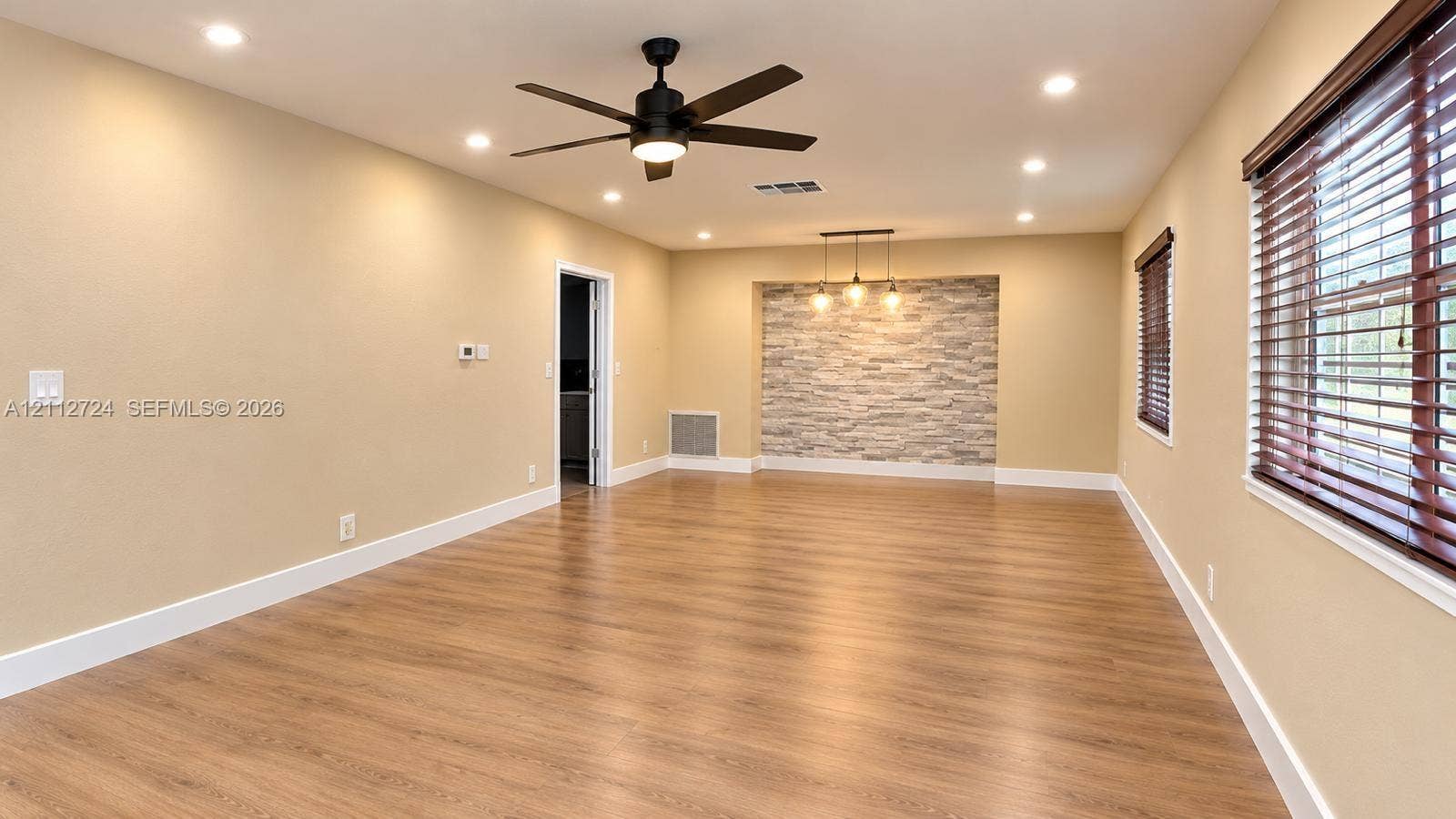 Interior space featuring wood-finish flooring, recessed lighting, a stone-accent wall with pendant fixtures, and a matte black ceiling fan