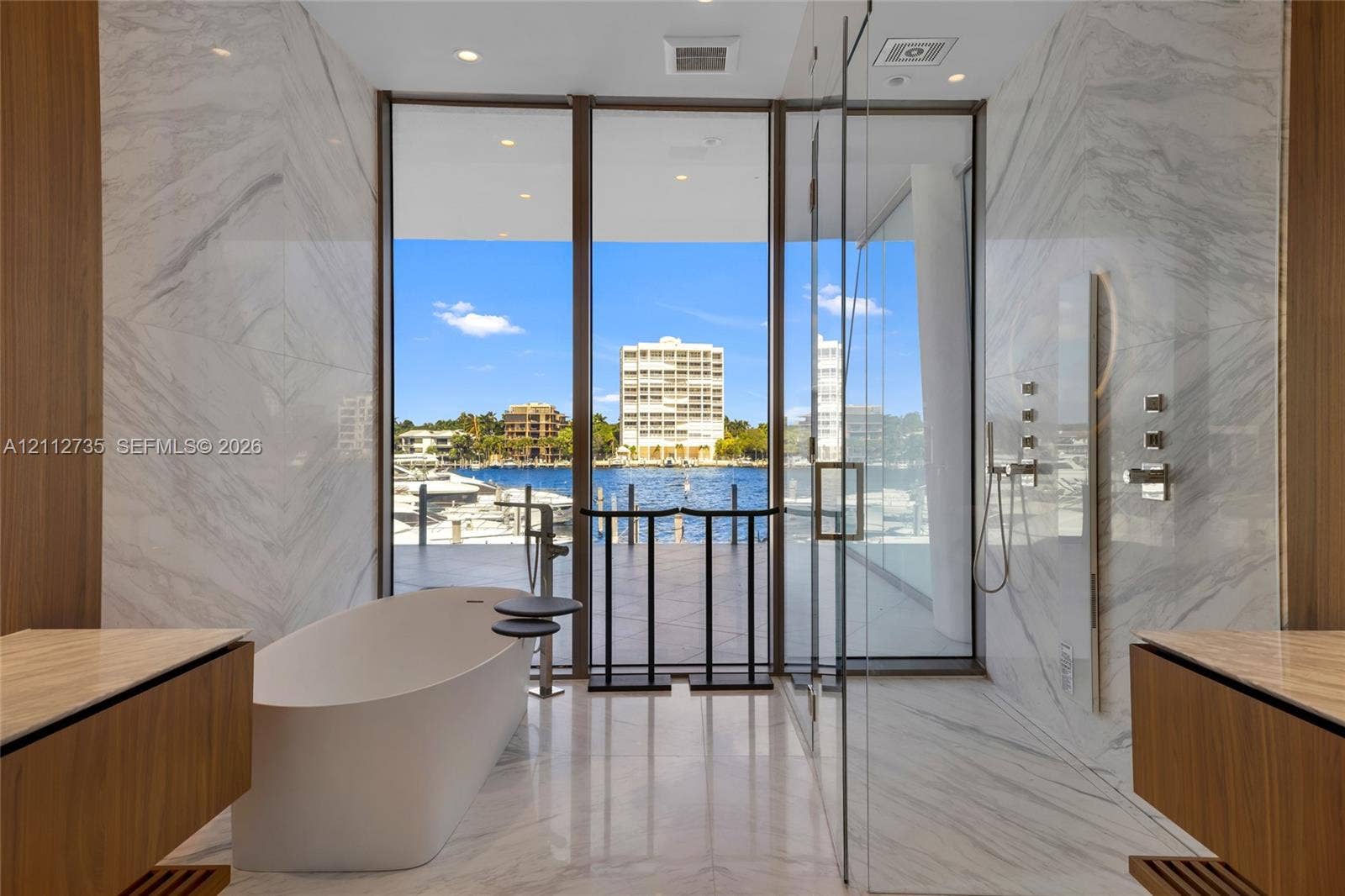 5 Grove Isle Drive, #S203, Coconut Grove, FL 33133 Floor-to-ceiling glass windows, stone-finish wall cladding, freestanding soaking tub, glass-enclosed shower, and dual wood-finish floating vanities